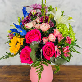 Mixed bouquet in a pink vase with roses, lilies, and bright accent flowers