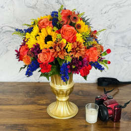 Colorful bouquet of roses, sunflowers, and mixed blooms in a gold vase