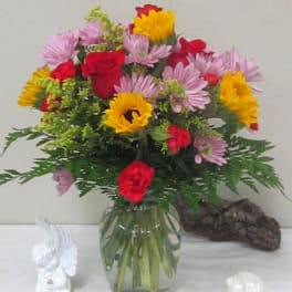 Mixed bouquet of red roses, pink daisies, and yellow flowers in a glass vase