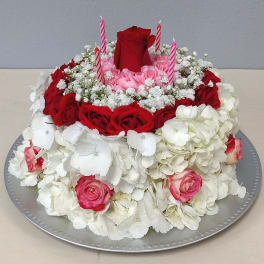 Round floral cake with red and pink roses and white hydrangeas, topped with candles
