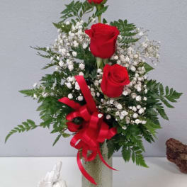 Three red roses in a glass vase with baby's breath and a red ribbon