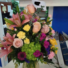 Mixed bouquet of pink lilies, roses, hydrangea, and colorful filler flowers in a glass vase