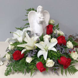 White lilies and red roses arranged around a white angel figurine