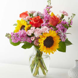 Bouquet of sunflowers, roses, and pink flowers in a clear glass vase