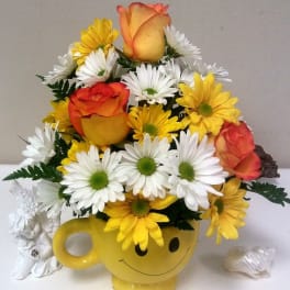 Yellow smiley-face mug filled with daisies and orange roses