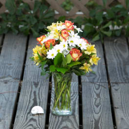 Bouquet of orange roses, white daisies, and yellow flowers in a clear glass vase