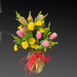 Pink tulips and yellow chrysanthemums in a glass vase with a red ribbon