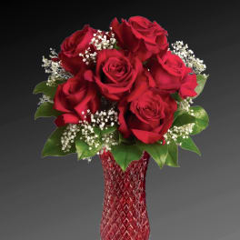 Red roses arranged in a red glass vase with white filler flowers