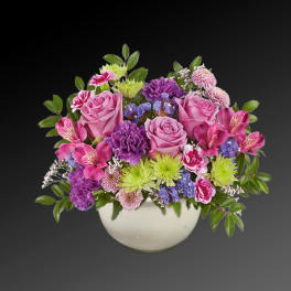 Pink and purple mixed flower arrangement in a white bowl vase
