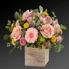 Pastel pink and yellow flower arrangement in a rustic wooden cube container