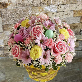 Basket arrangement of pink roses, daisies, and carnations with pastel eggs