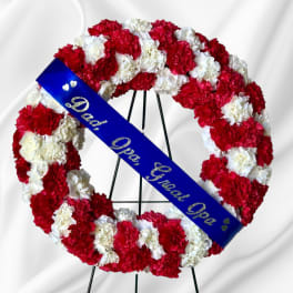 Red and white carnation funeral wreath with a blue memorial sash
