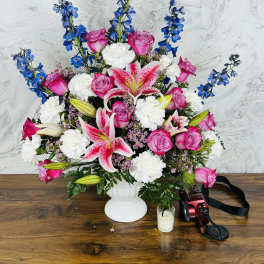 Pink roses and lilies in a white vase with blue delphinium and white carnations