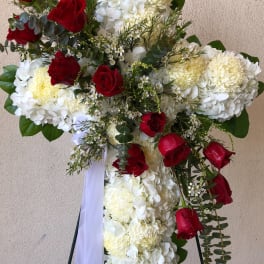 Cross-shaped floral tribute with white blooms and red roses on a stand