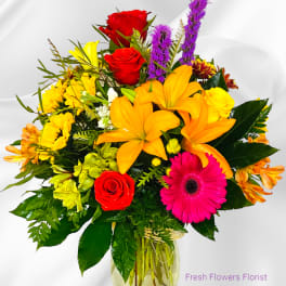Mixed bouquet of roses, lilies, and gerbera daisies in a glass vase