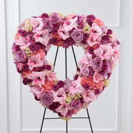 Heart-shaped floral wreath in pink and lavender tones on a black stand