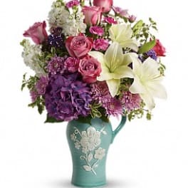 Mixed bouquet of pink, purple, and white flowers in a teal vase