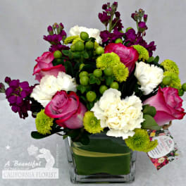 Pink roses, white carnations, and purple stock in a square glass vase