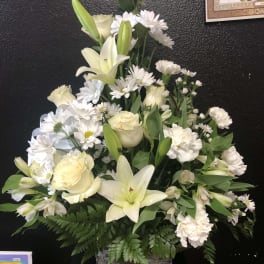 White lilies and roses arranged in a wicker basket with white daisies