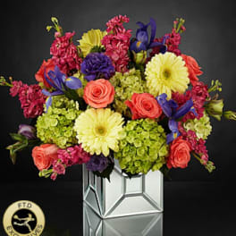 Colorful bouquet of roses, gerbera daisies, and purple blooms in a mirrored vase