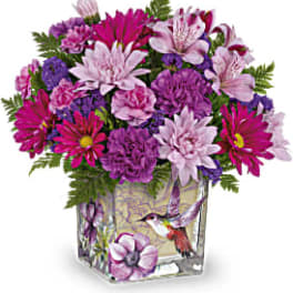 Pink and purple mixed bouquet in a square glass vase with a hummingbird design