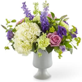 Purple and white mixed flower arrangement in a gray pedestal vase