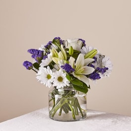White lilies and daisies in a clear glass vase with purple filler flowers