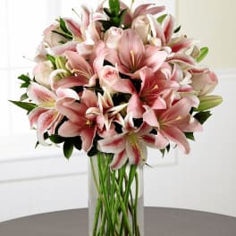Pink lilies and roses arranged in a clear glass vase
