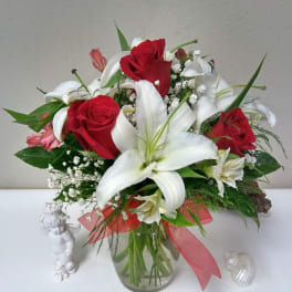 Bouquet of red roses and white lilies in a glass vase with a pink ribbon
