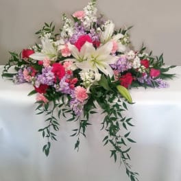 Casket spray with white lilies, pink and purple flowers, and trailing greenery