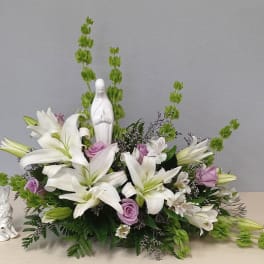 White lilies and lavender roses arranged around a small white statue