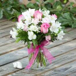 Pink roses and white alstroemeria in a glass vase with a pink ribbon