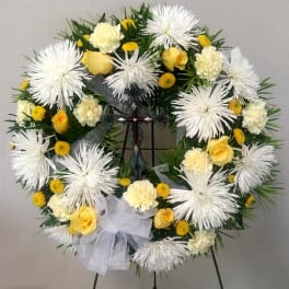 White and yellow floral wreath on a stand with a white bow