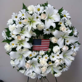 White floral wreath with lilies, daisies, and roses around an American flag