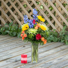 Colorful mixed flower arrangement in a tall glass vase with a red candle nearby