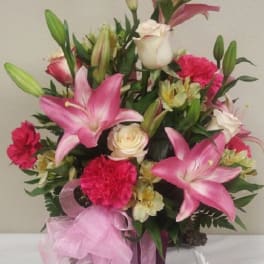 Pink lilies and carnations in a purple vase with a pink ribbon