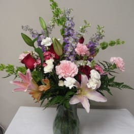 Mixed bouquet of lilies, roses, carnations, and purple spikes in a glass vase