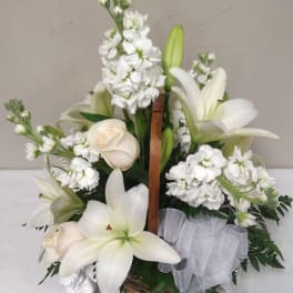 White lilies and white flowers arranged in a basket with a sheer ribbon