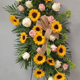 Standing floral spray with sunflowers, pink and white roses, and a burlap bow