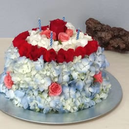 Tiered floral cake with red roses, blue hydrangeas, and striped candles