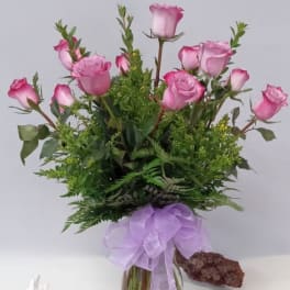 Pink roses in a glass vase with a lavender ribbon bow