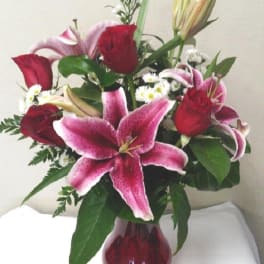 Bouquet of red roses and pink lilies in a red glass vase