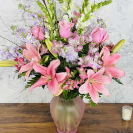 Pink lilies and roses arranged in a frosted glass vase