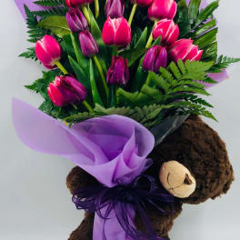 Bouquet of pink and purple tulips wrapped with purple paper, held by a teddy bear
