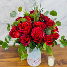 Red roses arranged in a white vase with greenery