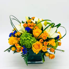 Orange roses and white lilies in a square glass vase