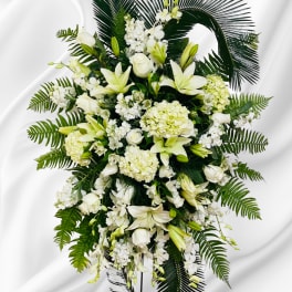 White floral standing spray with lilies and hydrangeas on dark palm fronds