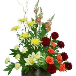 Mixed floral arrangement in a dark round vase with lilies and dahlias