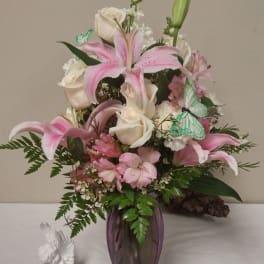 Pink lilies and white roses arranged in a purple vase with butterfly picks