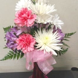 Pink and white carnations in a pink glass vase with a ribbon